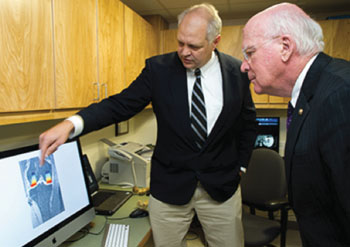 Imagen: El profesor de investigación musculo-esquelética de la Universidad de Vermont, Bruce Beynnon, PhD, a la izquierda, describe como la Universidad de Vermont usa su máquina de investigación de RM para la investigación de las lesiones de rodilla, al Senador de los EE.UU, Patrick Leahy (Fotografía cortesía de COM Design & Photography).