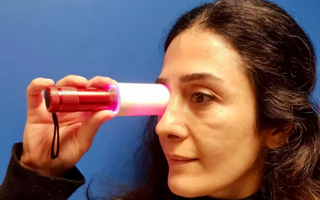 Image: Study co-author Dr. Pardis Kaynezhad holds a deep red light over her eye to stimulate the mitochondria in her retinal cells. (Photo courtesy of UCL)