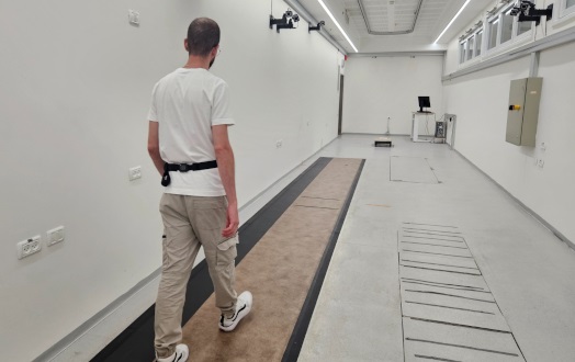 Image: A person walking in a state-of-the-art gait lab, with a wearable sensor positioned on his lower back (Photo courtesy of Tel Aviv University)