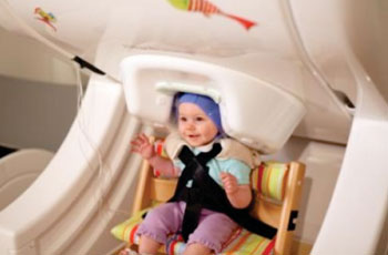 Image: A one-year-old baby sits in a brain scanner, called magnetoencephalography (MEG)—a noninvasive approach to measuring brain activity. The baby listens to speech sounds such as “da” and “ta” played over headphones while researchers record her brain responses (Photo courtesy of the Institute for Learning & Brain Sciences at the University of Washington).