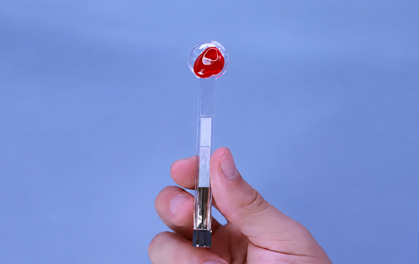Image: The red, peach-flavored candy coating on Lollylab stimulates saliva production, and a sensor at the bottom analyzes it for acetaminophen. (Image Credit: Adapted from ACS Sensors 2026, DOI: 10.1021/acssensors.6c00691)