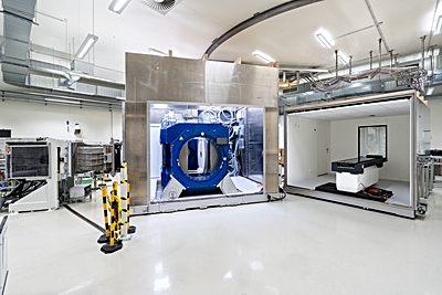 Image: Beam line of the proton therapy system (left) with opened Aurora-PT system, i.e. in-beam MRI (middle) and patient couch (right) (Photo courtesy of UKD/Kirsten Lassig)