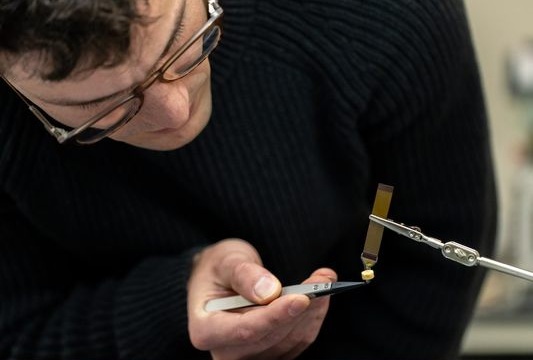 Image: PhD Innovation Fellow Jonathan \"Jono\" Pelusi examines the neural device designed to promote healing of the skull following implantation onto the brain (Photo courtesy of Robert Anderson)